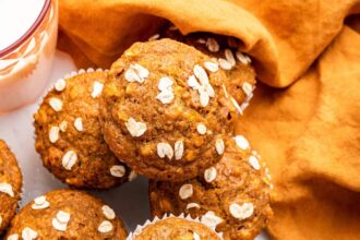 Multiple pumpkin muffins near one another with some stacked on top of others.