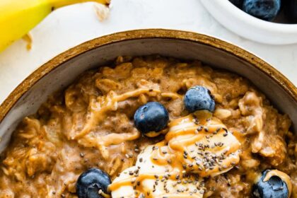 A bowl of peanut butter oatmeal topped with fresh banana slices, blueberries, a drizzle of peanut butter and chia seeds.