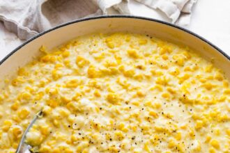 Creamed corn served in a white skillet with a silver spoon topped with freshly cracked pepper.