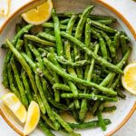 Roasted green beans in a large bowl with lemon wedges.