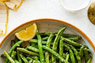 Roasted green beans in a large bowl with lemon wedges.