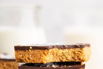 Four peanut butter bars stacked on top of each other on a wire cooling rack. The top bar has a bite taken out of it.