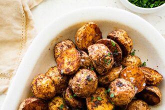 Crispy air fryer potatoes on a white plate garnished with fresh herbs and flaky sea salt.