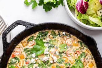 An egg white frittata in a cast iron skillet. The frittata is garnished with fresh herbs and feta cheese.