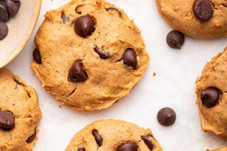 Multiple chocolate chip protein cookies are spread out on a countertop.