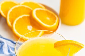 An adrenal cocktail in a glass with a clear straw in it. An orange slice is on the edge of the glass.