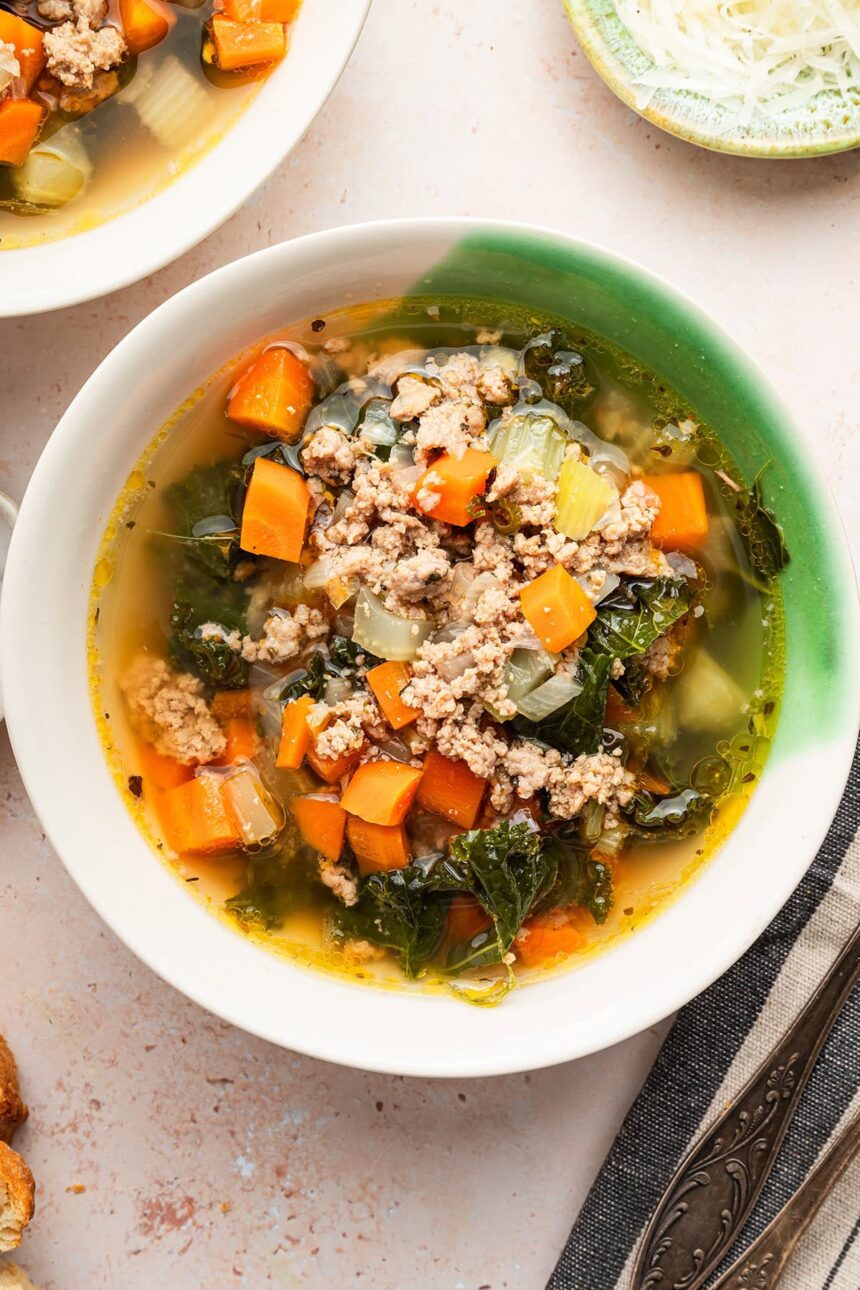 Sausage and kale soup served up in a green and white soup bowl.