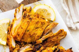 Chicken Shawarma sliced on a cutting board. There is a knife and lemon slices next to the chicken.