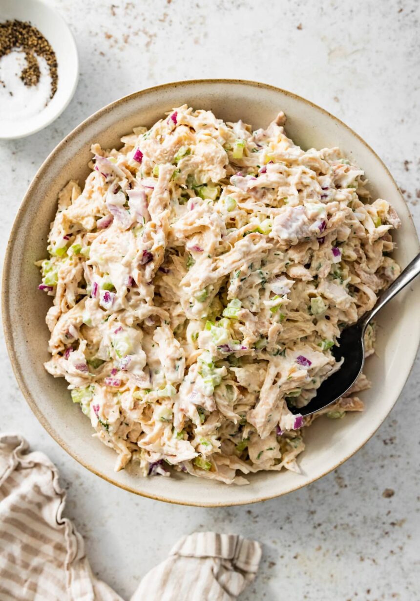 Cottage cheese chicken salad served in a cream bowl with a spoon. There is a small bowl with salt and pepper next to it.