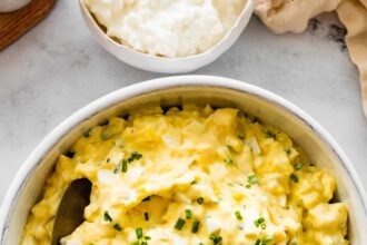 Cottage cheese egg salad served in a white ceramic bowl served with a silver spoon. Fresh chives are topping the egg salad.