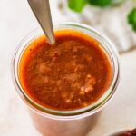 A glass weck jar filled with homemade red enchilada sauce. There is a silver spoon in the glass jar.