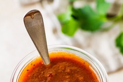A glass weck jar filled with homemade red enchilada sauce. There is a silver spoon in the glass jar.