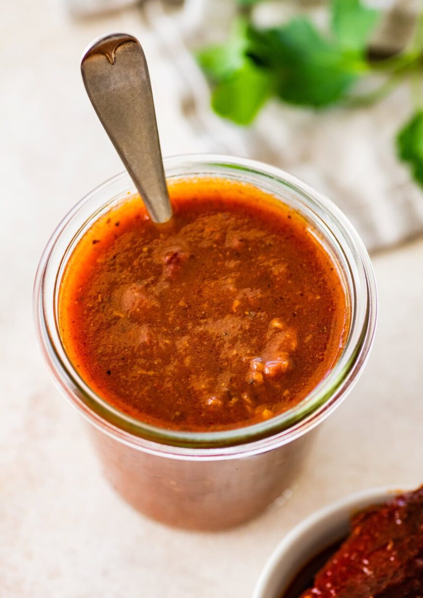 A glass weck jar filled with homemade red enchilada sauce. There is a silver spoon in the glass jar.