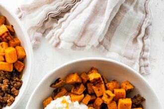 Ground beef, roasted sweet potatoes, cottage cheese and chopped avocado in a white bowl topped with a drizzle of honey.