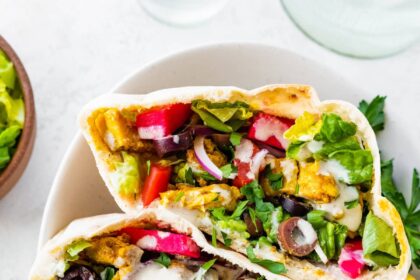 Three halves of chicken shawarma pita pockets stacked in a bowl, filled with veggies, olives, pickled turnips, and topped with yogurt sauce and fresh parsley.